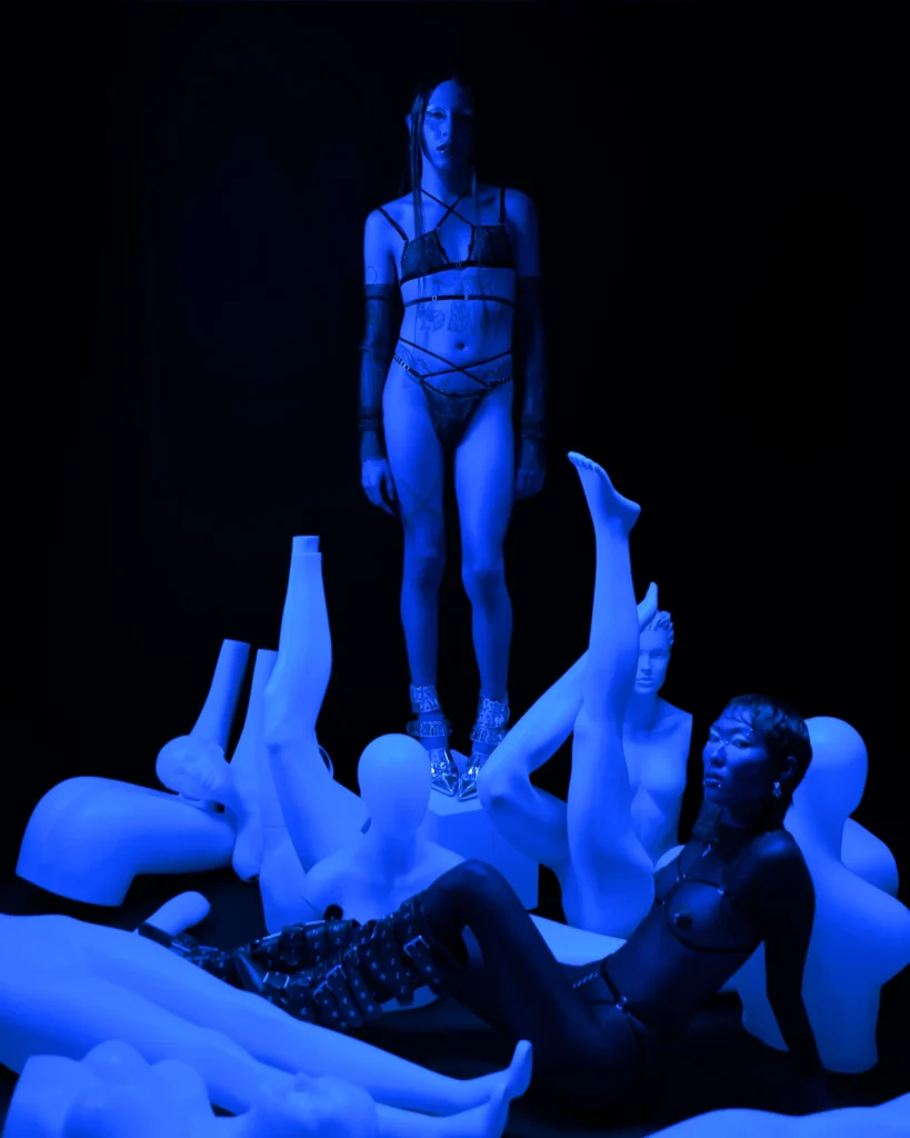 Avant-garde fashion editorial with models in strappy lingerie and mannequins under dramatic blue lighting
