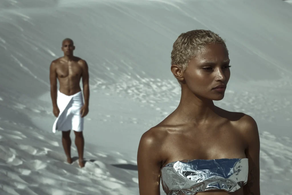 Fashion editorial with woman in metallic top and man in white wrap on white sand dunes