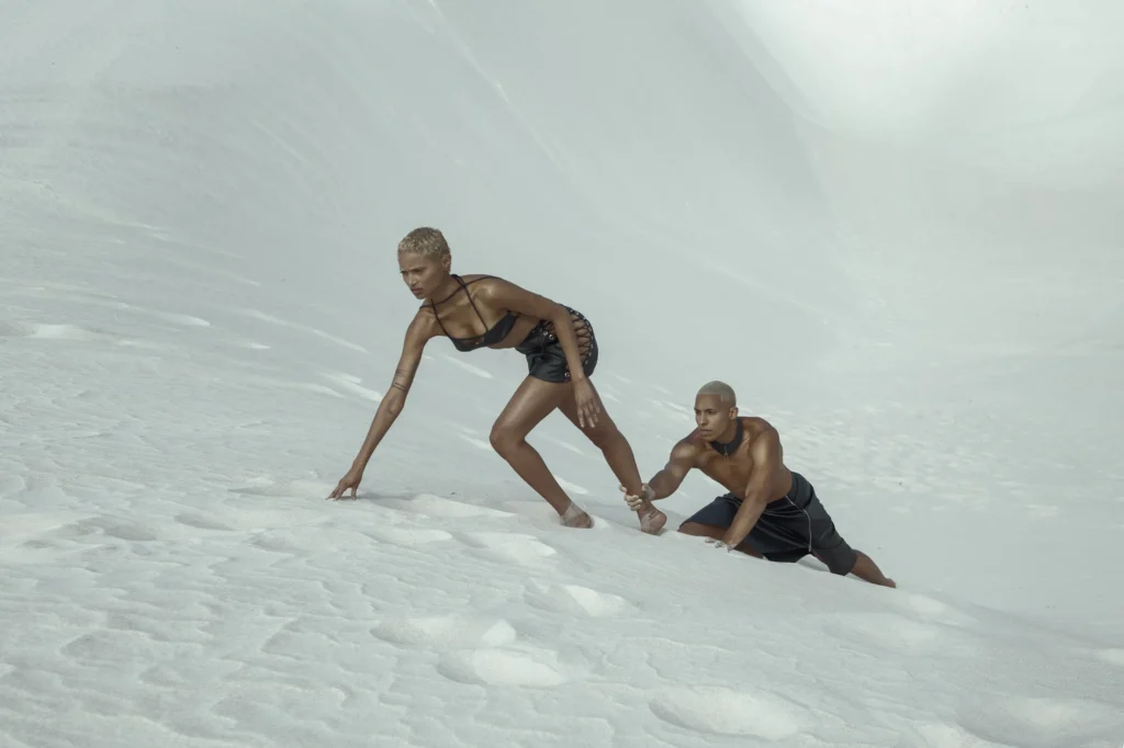 Two models in black swimwear posing on white sand dunes, editorial fashion shoot Berlin