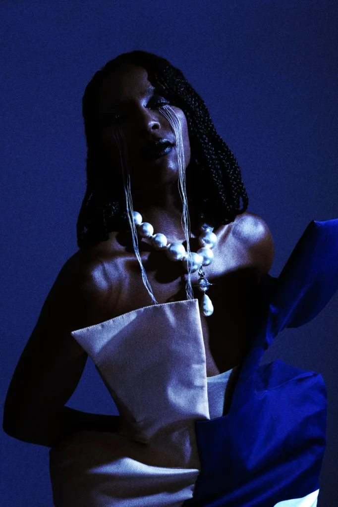 Woman with braids wearing oversized pearl necklace in dramatic blue studio lighting, fashion editorial