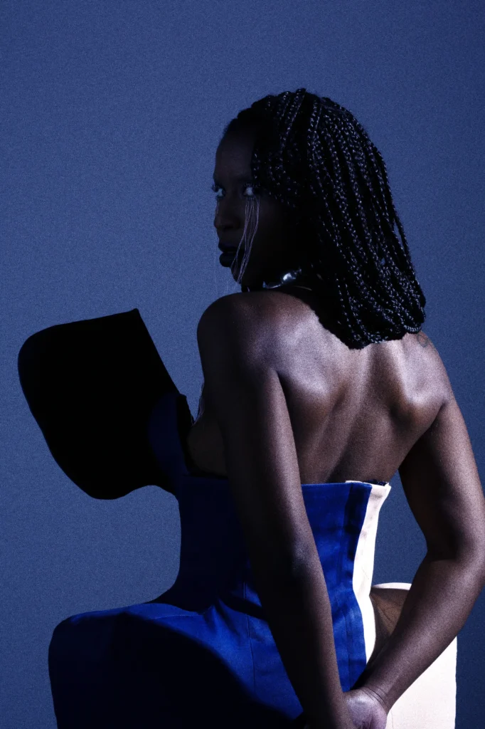 Woman with braids wearing sculptural blue corset, artistic fashion portrait against blue background