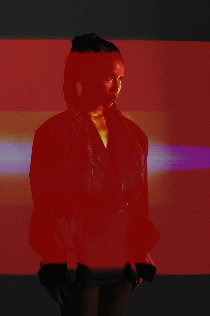 Woman in sheer robe with dramatic red and orange light projection, artistic fashion portrait Berlin