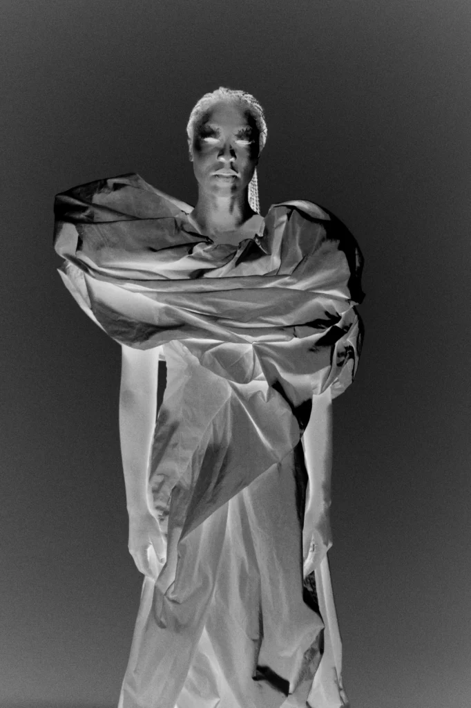 Model wrapped in sculptural crumpled paper garment, dramatic black and white fashion portrait with statement earring