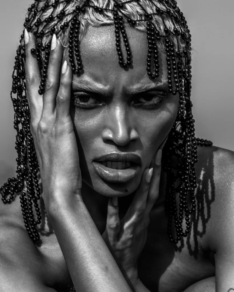Woman with beaded headpiece in dramatic black and white artistic portrait, hands framing face
