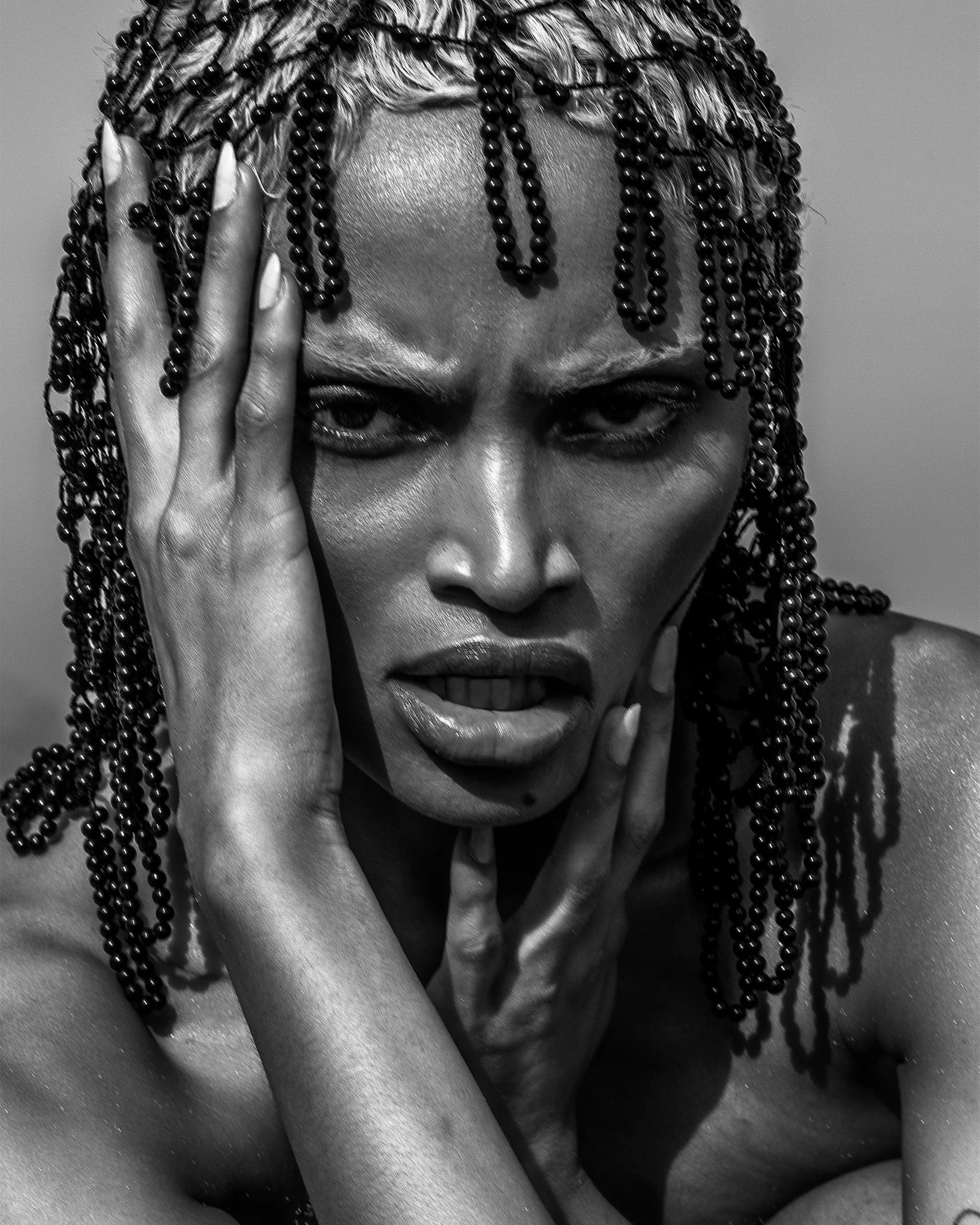 Woman with beaded headpiece in dramatic black and white artistic portrait, hands framing face