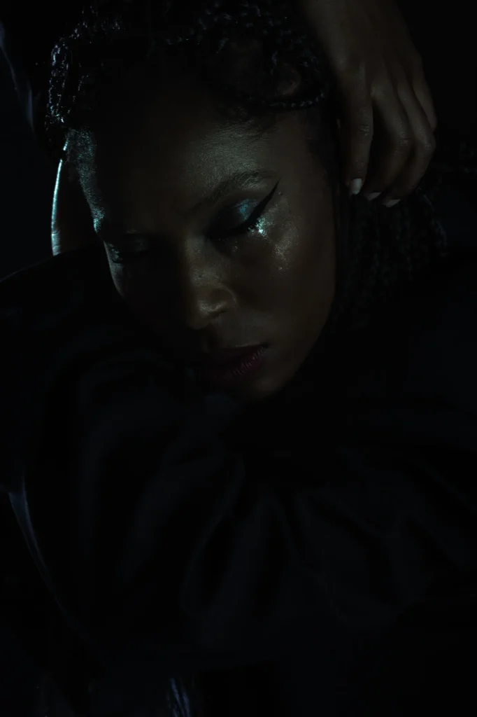 Woman with braided hair and glitter eye makeup in moody dramatic lighting, downward gaze