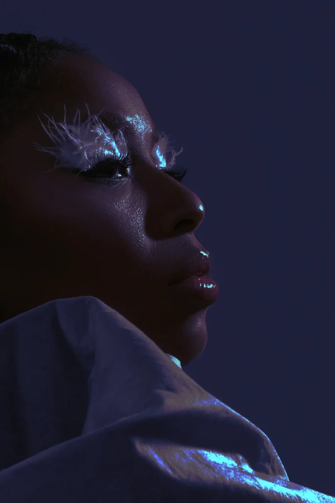 Woman with ethereal white feather eye makeup and glossy lips in dramatic blue studio lighting