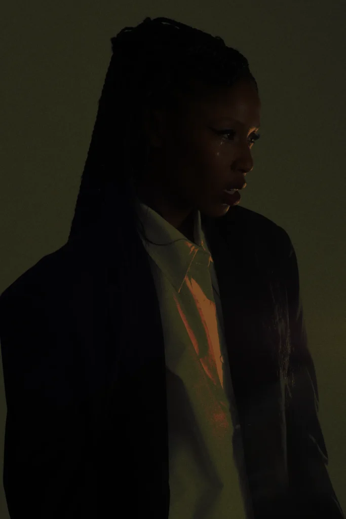 Woman with long braids in dark blazer and button-up shirt, moody dramatic studio lighting