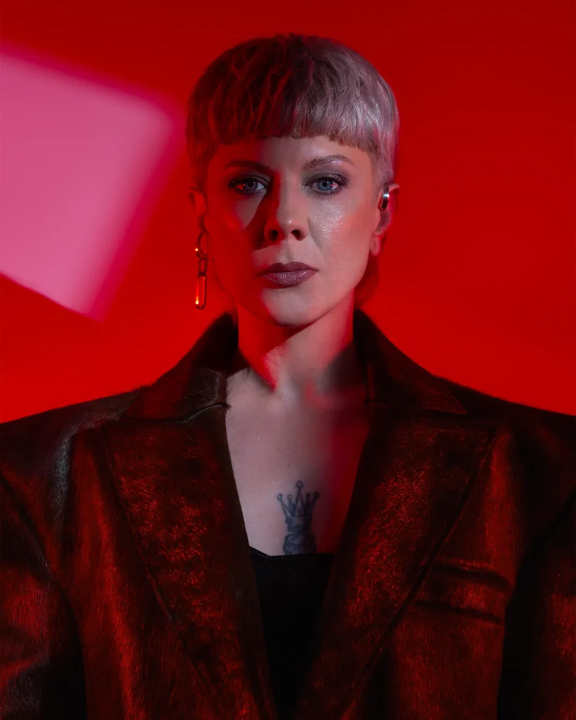 Woman with short platinum hair and crown chest tattoo in red leather blazer, dramatic red studio lighting